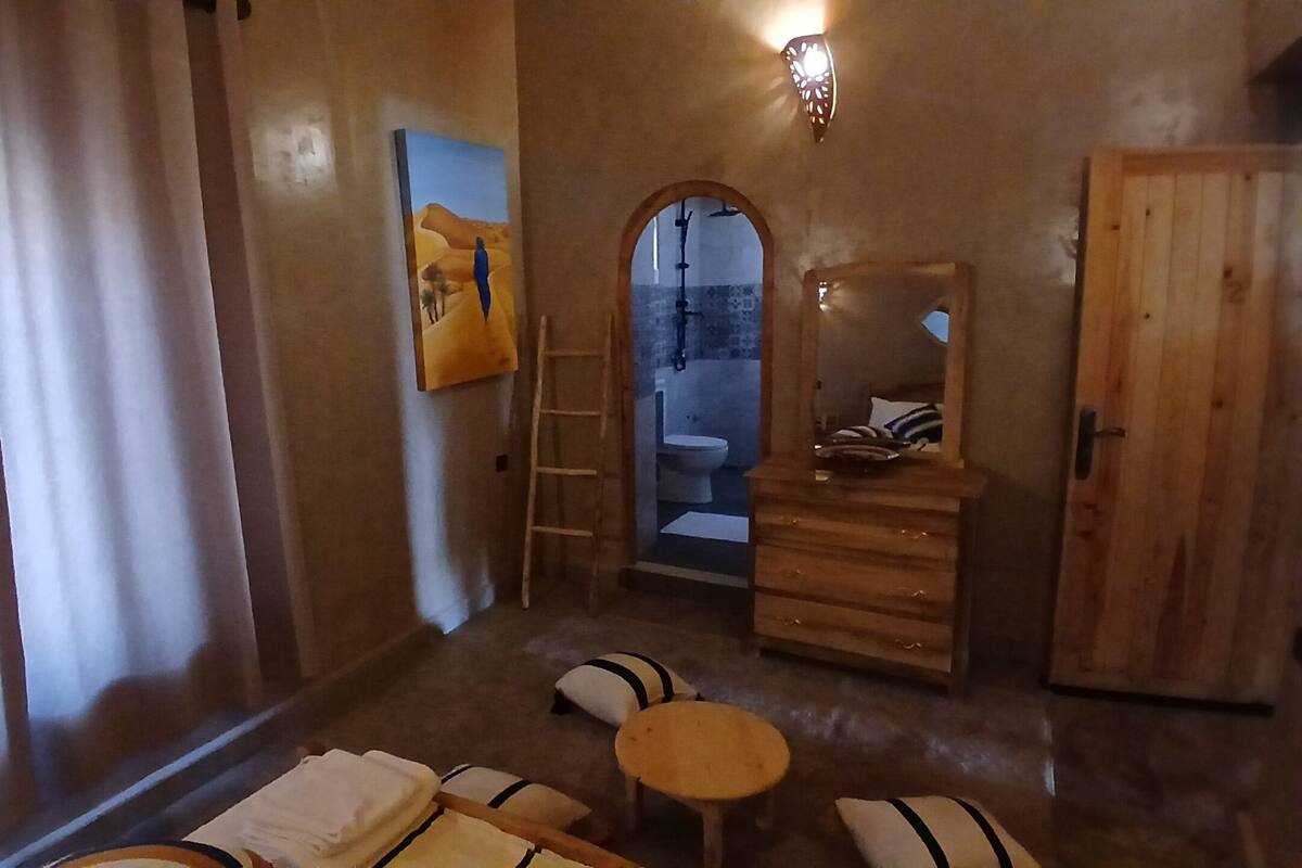 Una habitación con un aparador de madera, un espejo, una mesita redonda pequeña, un banco y un cuadro en la pared.