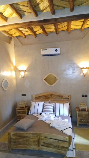 A bedroom with a wooden bed, two bedside tables, a wall-mounted air conditioner, and two wall-mounted lights.
