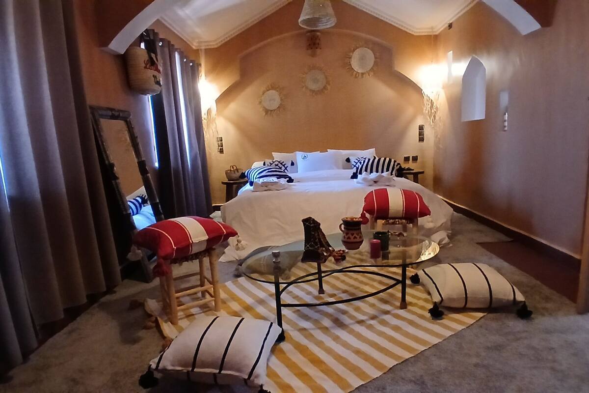 Una habitación de hotel con una cama, una mesita de vidrio, una silla y un tapete a rayas.