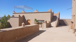 A building with a flat roof, a wooden door, and a staircase leading to an upper level. - La Colline Verte Dar Ait El Abass  (Skoura)