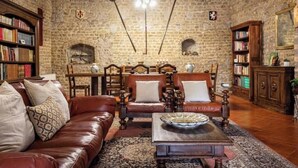 A room with a stone wall, leather sofa, wooden chairs, a coffee table, and bookshelves. - Corte San Pastore - Boutique Location di Charme Senza Tempo (Tivoli)