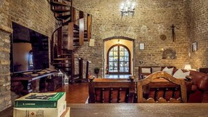 A library with bookshelves, a wooden staircase, and a large arched window. - Corte San Pastore - Boutique Location di Charme Senza Tempo (Tivoli)