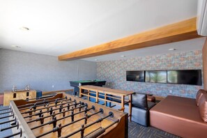 A room with a foosball table, a pool table, a sofa, and a television mounted on the wall. - Casa Oasis - Upscale 3B/3B condo (Cabo San Lucas)