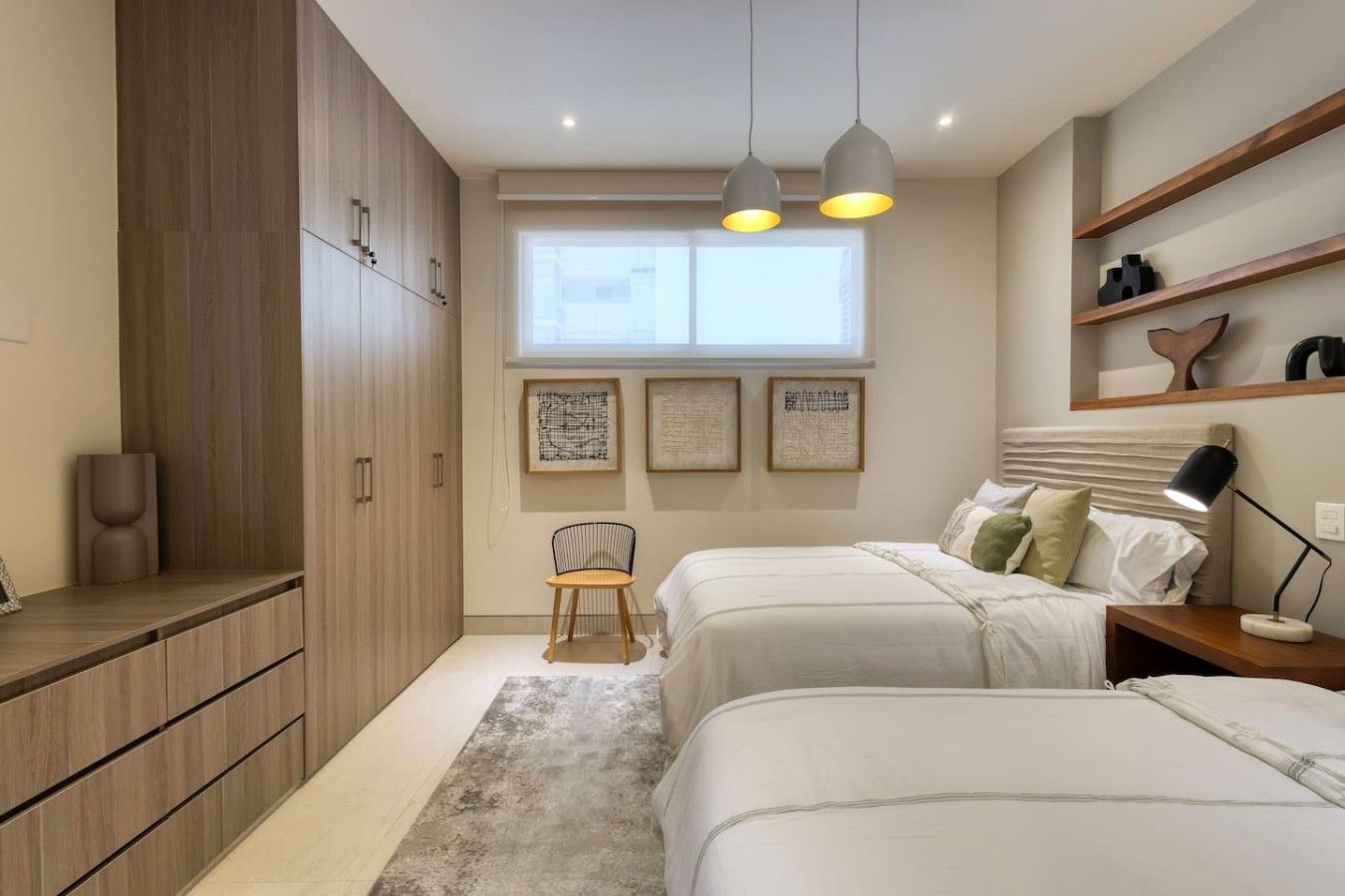 Ein Schlafzimmer mit zwei Betten, einem Sessel, einem Schreibtisch, einem Fenster und Wandregalen.
