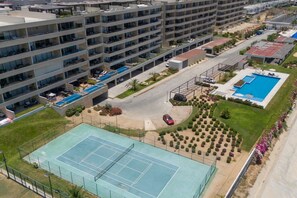 Ein mehrstöckiges Wohngebäude mit Tennisplatz, Schwimmbad und Parkbereich.