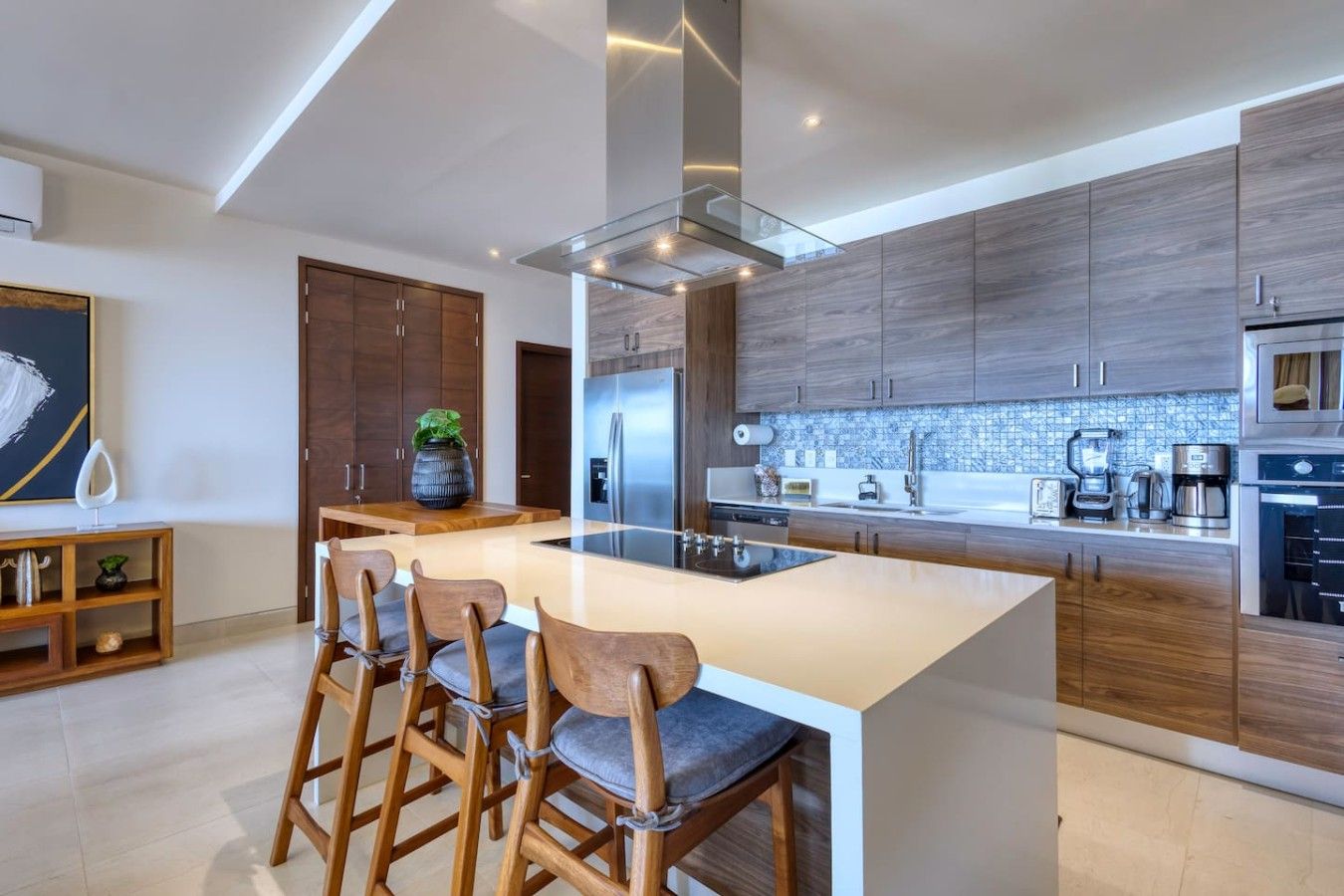 Eine moderne Küche mit einer zentralen Kochinsel, Barhocker, Holzschränken und einem eingebauten Backofen.