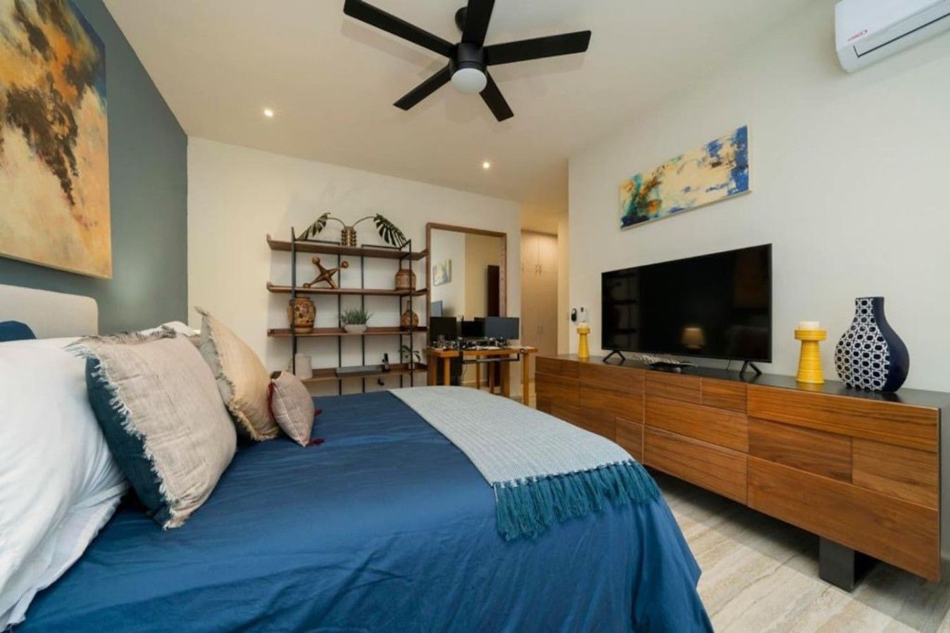 A modern bedroom with a bed, a TV, a wooden dresser, and a ceiling fan.