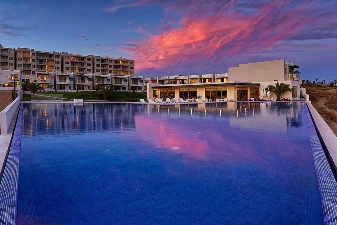 Ein Schwimmbad mit Blick auf Hotelgebäude und einem Sonnenuntergangshimmel.