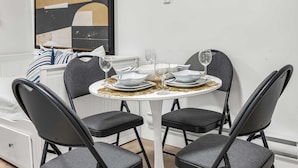 Un comedor con una mesa redonda, cuatro sillas y una pared blanca con un cuadro.