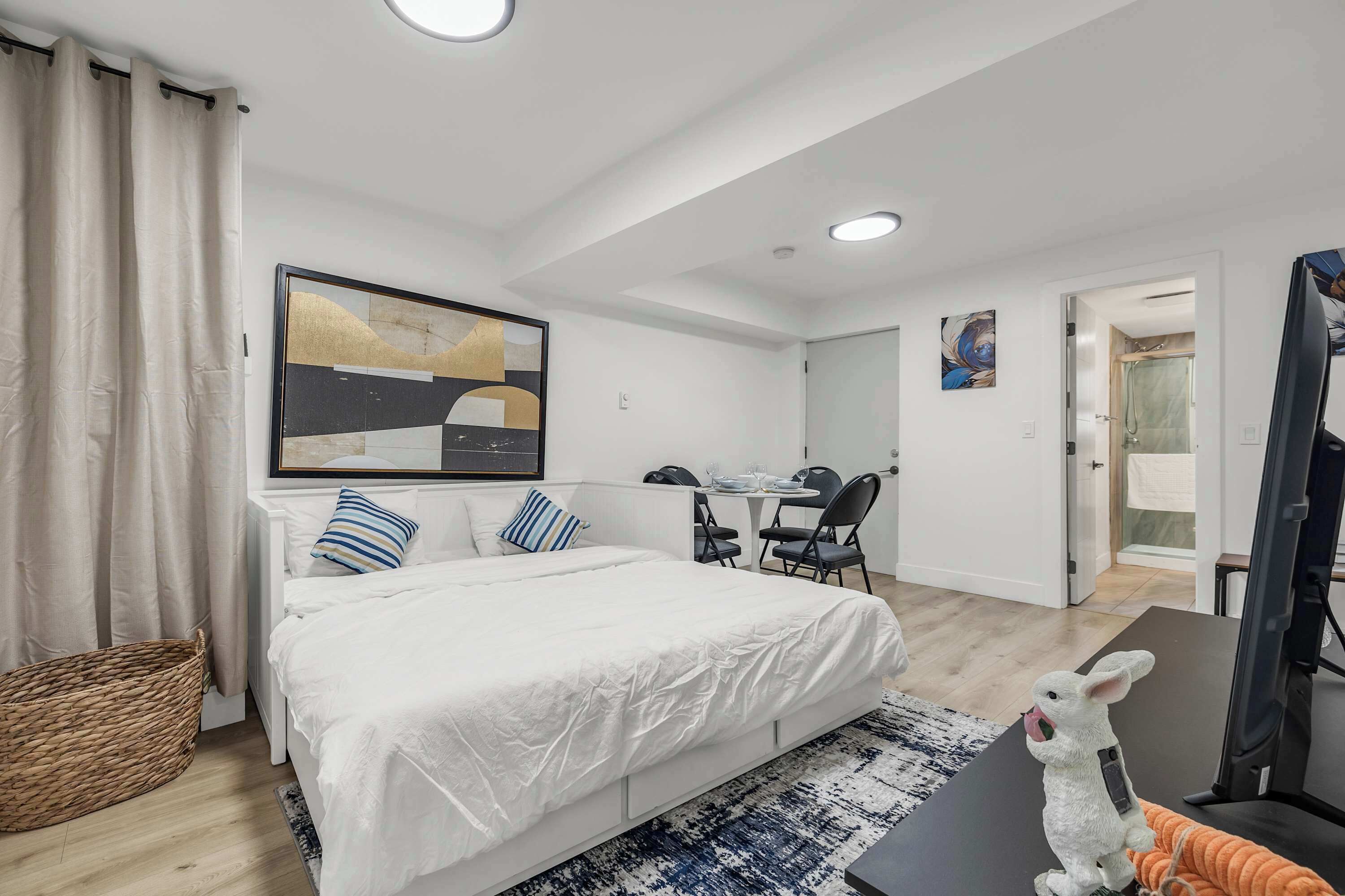 A modern hotel room with a large bed, a desk, and a chair, a small table, and a decorative rabbit figurine.