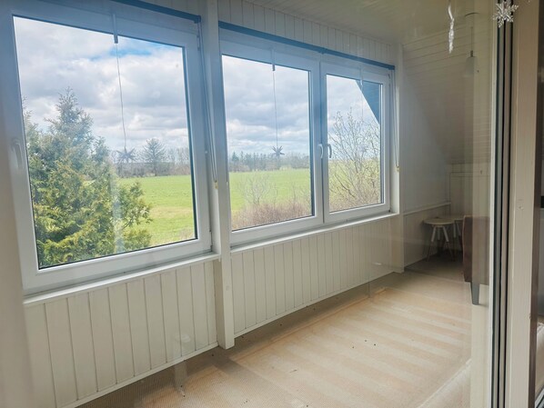 A room with large windows, a wooden floor, and a view of a green field. - Family private house 4-5 rooms (Brovst)