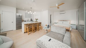 Quarto moderno e bem iluminado, com cozinha compacta, área de jantar, cama e ventilador de teto.