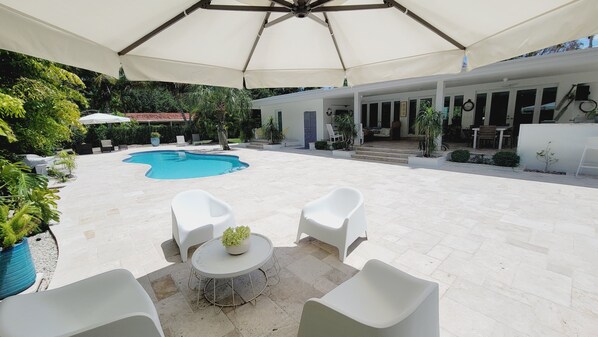 A pool area with white outdoor furniture, a covered seating area, and a building with large windows.