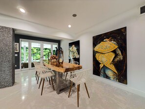 A modern dining area with a wooden table, white chairs, and a large painting on the wall.