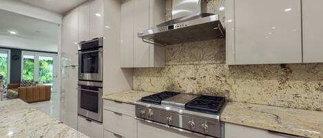 A modern kitchen with stainless steel appliances, marble countertops, and a view of the outdoors.