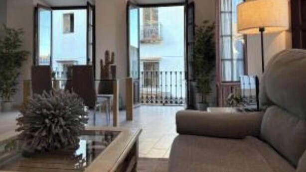 A modern living room with a sofa, a coffee table, and a lamp. There is a balcony visible through the open door.
