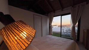 A bedroom with a bed, a large lamp, a window with curtains, and a view of the outside.