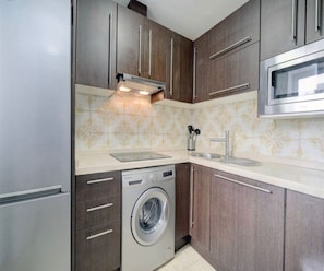 Una cocina funcional con lavadora, electrodomésticos de acero inoxidable y un salpicadero decorativo.