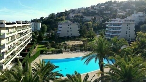 A hotel with a pool, palm trees, and a view of a hillside. - Apartment with swimming pool, janitor and parking space (Mandelieu-la-Napoule)