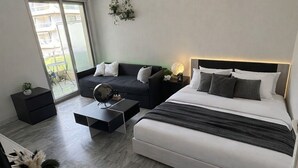 A modern bedroom with a bed, a sofa, a coffee table, and a hanging light fixture. - Apartment with swimming pool, janitor and parking space (Mandelieu-la-Napoule)