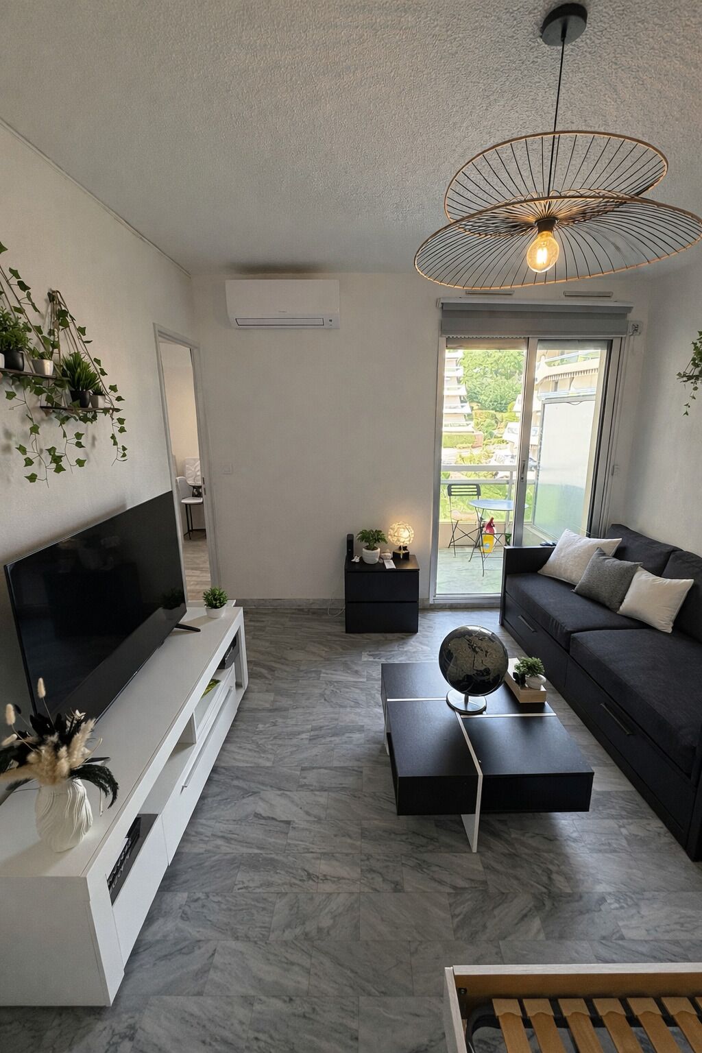 A modern living room with a flat-screen TV, a black sofa, a coffee table, and a hanging light fixture.