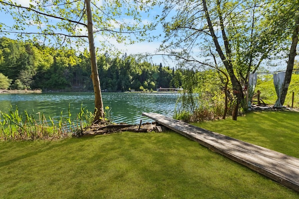Une vue sur le lac, avec un quai en bois, une zone herbeuse et des arbres.