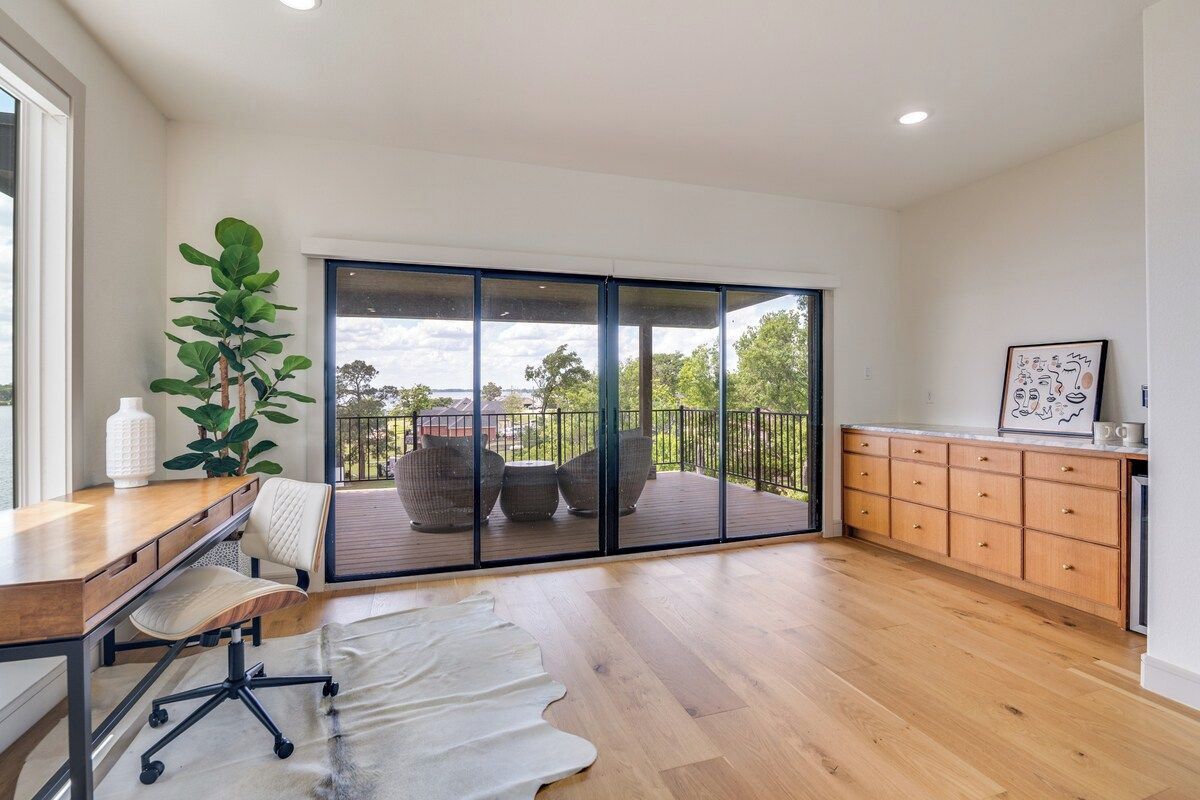 A spacious room with a wooden floor, a desk with a chair, a large sliding glass door leading to an outdoor deck, and a cabinet with drawers.