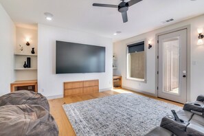 Een moderne woonkamer met een flatscreen televisie, een plafondventilator en een groot raam.