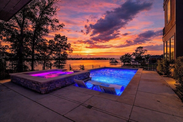 Une piscine entourée de pierres et dotée de sièges intégrés, le tout mis en valeur par le décor d’un coucher de soleil.