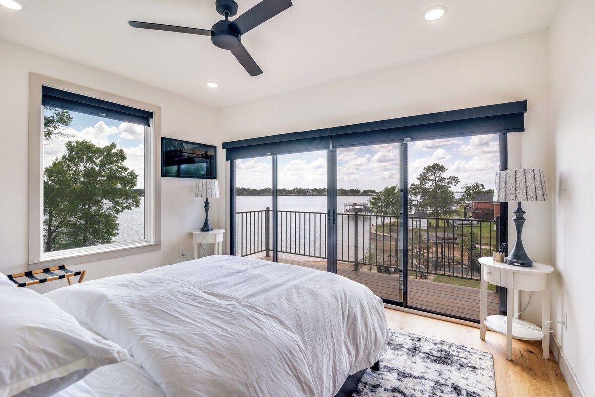Un dormitorio con una cama grande, ventilador de techo, televisor y balcón con vistas al exterior.