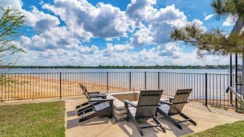 Un espace extérieur aménagé avec des chaises et une table, offrant une vue sur une étendue d’eau et une côte lointaine.
