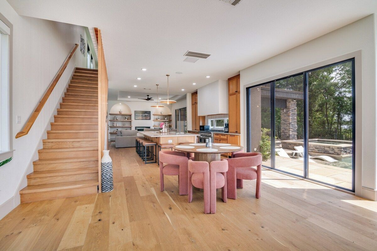 Una cocina moderna con una isla central, escalera de madera y grandes puertas correderas de vidrio que dan a un área exterior.