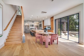 Une cuisine moderne dotée d’un îlot central, d’un escalier en bois et de grandes portes-fenêtres coulissantes donnant sur un espace extérieur.
