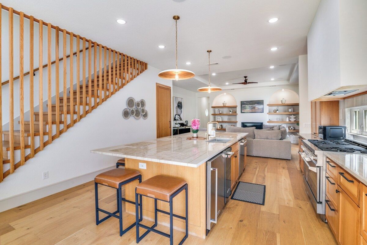 Une cuisine moderne dotée d’un îlot central, de tabourets de bar, d’un escalier en bois et d’un coin repas avec un canapé.