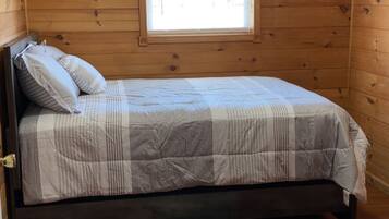 Ein Zimmer mit Holzwänden, einem Bett, einem Fenster mit weißem Vorhang und einer Deckenleuchte.