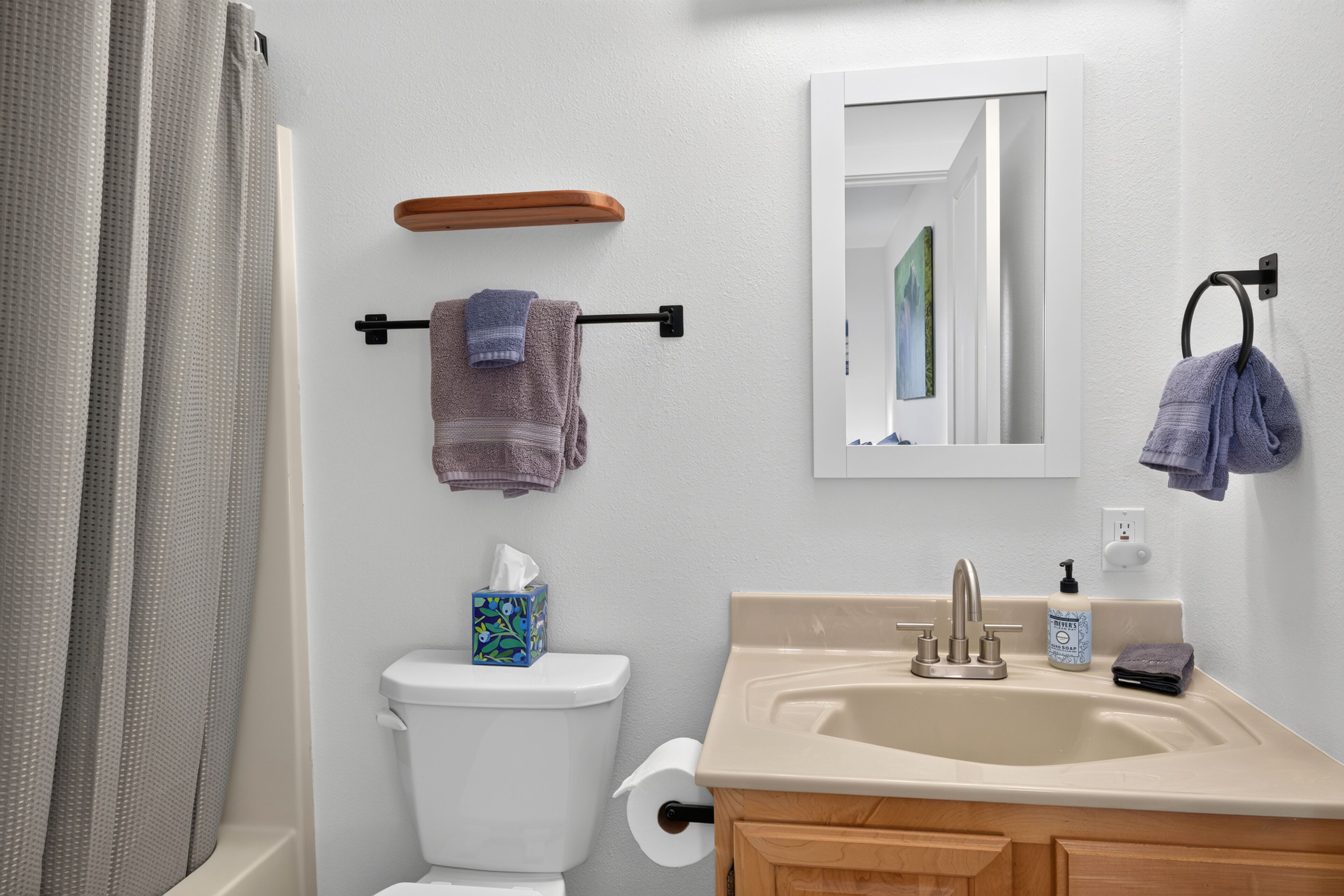 A bathroom with a toilet, sink, mirror, towel rack, and shower curtain.