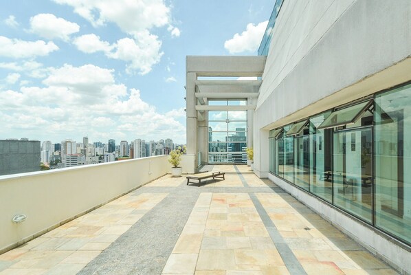 A rooftop terrace with a view of the city skyline, a seating area, and a glass wall.