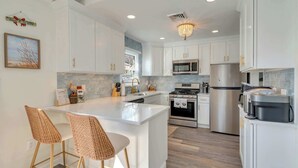 A kitchen with white cabinets, stainless steel appliances, a central island with bar stools, and a chandelier. - 2 BR Bay Breeze Retreat (Lower Township)