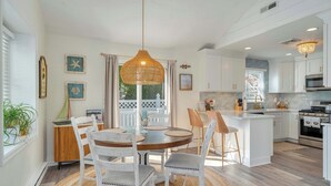 A modern kitchen with white cabinetry, a central island, and a dining area with a round table and chairs. - 2 BR Bay Breeze Retreat (Lower Township)