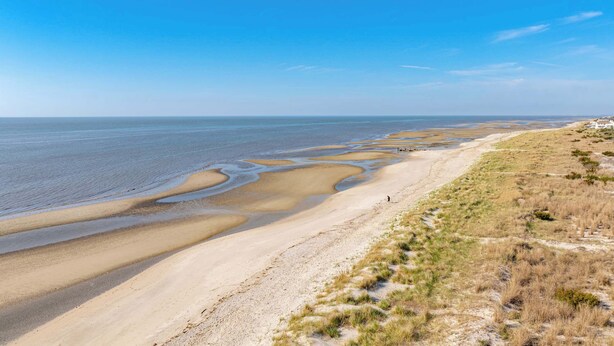 A coastal landscape with a sandy beach, a grassy dune area, and a clear blue sky. - 2 BR Bay Breeze Retreat (Lower Township)