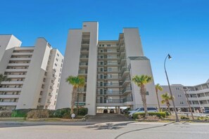 Un edificio residencial de varios pisos con balcones, una zona de estacionamiento y palmeras.