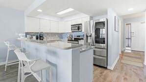 Cozinha moderna com armários brancos, eletrodomésticos de aço inoxidável e um espaço de bar com cadeiras brancas.