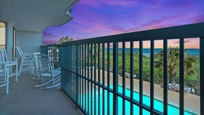 Uma varanda com vista para uma piscina e o oceano ao pôr do sol.