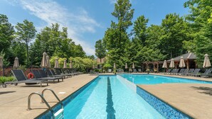 A swimming pool with lounge chairs and umbrellas, surrounded by trees.