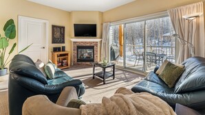 A living room with leather sofas, a fireplace, a flat-screen TV, and a large window with curtains.