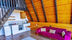 Moderni loft-tyylinen asunto, jossa on esillä olevat puupalkit, keittiöalue, violetti sohva ja portaikko.