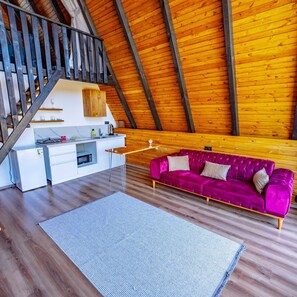 A modern loft with exposed wooden beams, a kitchen area, a purple sofa, and a staircase.
