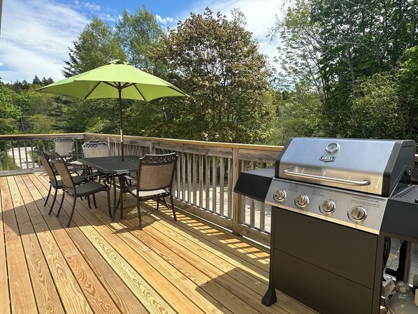 An outdoor deck with a grill, a table, chairs, and an umbrella.