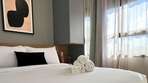 Una cama grande con sábanas blancas, un almohadón negro y una obra de arte abstracta enmarcada en la pared.