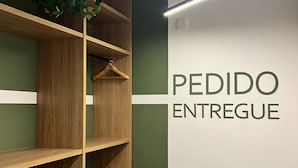 Una estantería de madera con una planta colgante, una pared con el texto 'PEDIDO ENTREGUE' y una lámpara moderna.